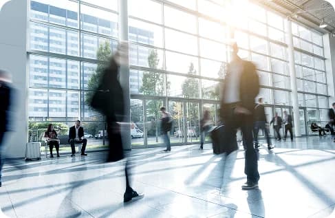 A bright glass office lobby with figures crossing it in motion